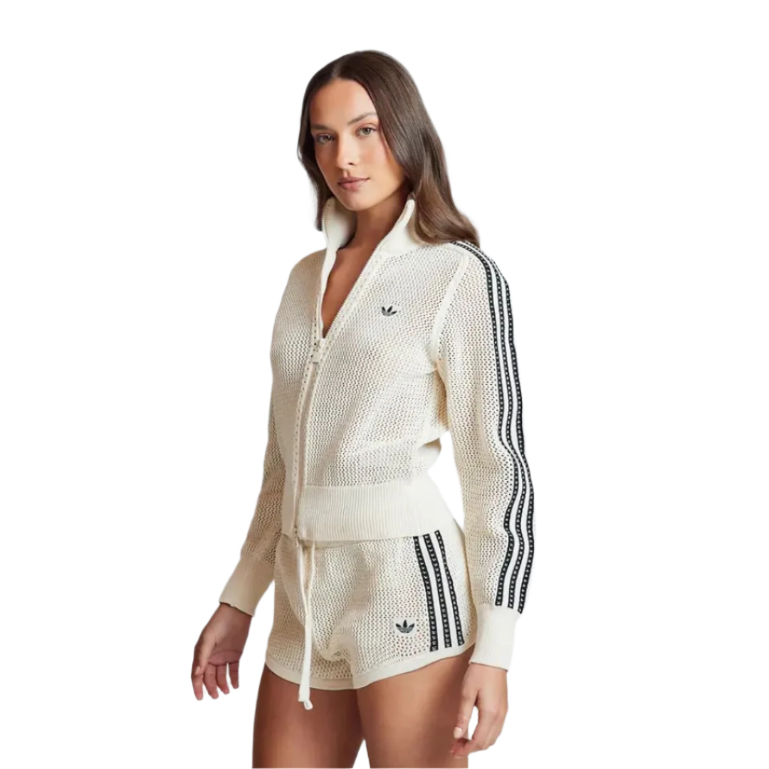 Woman wearing a cream-colored Adidas tracksuit with black stripes on a light gray background