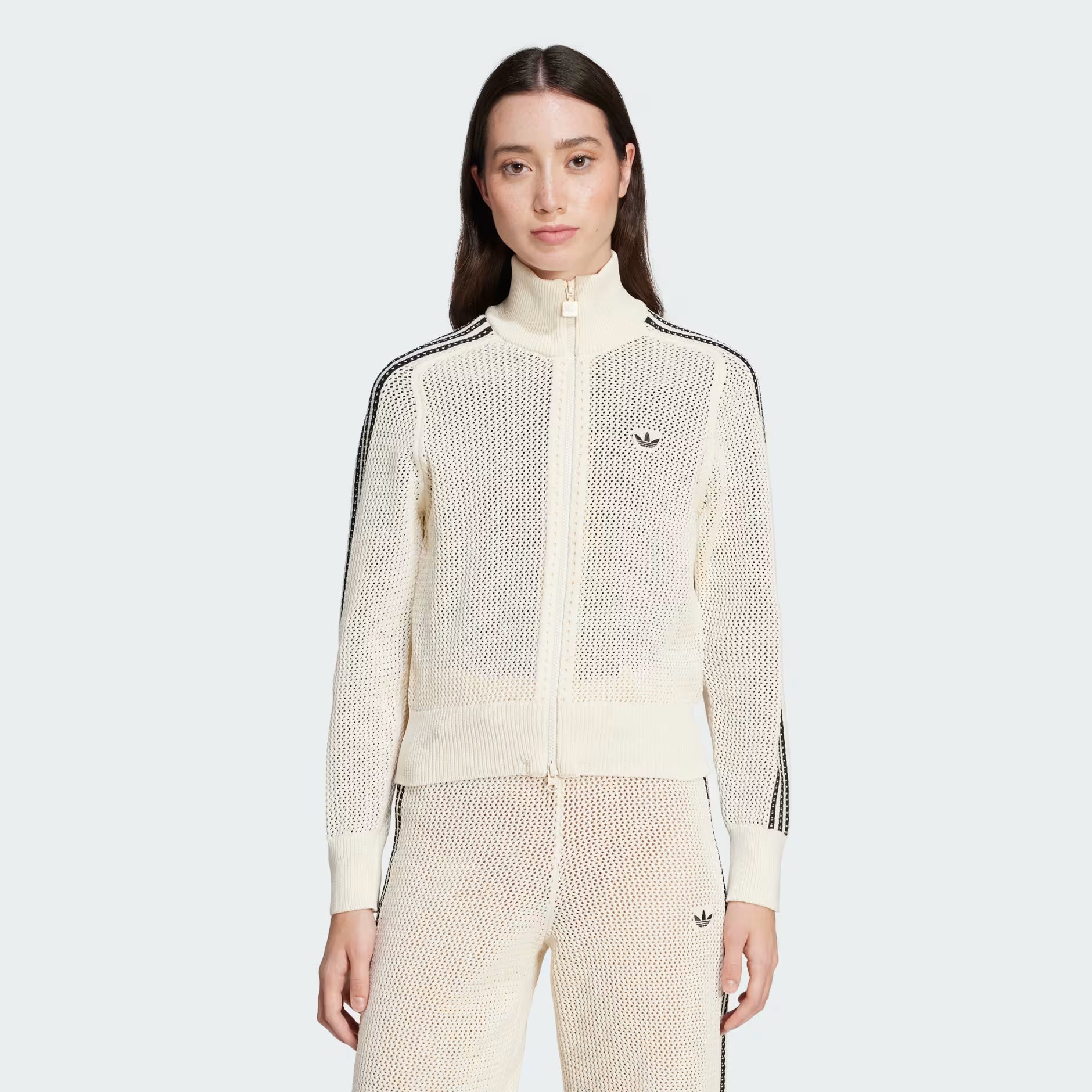Woman wearing a cream-colored Adidas tracksuit on a light gray background